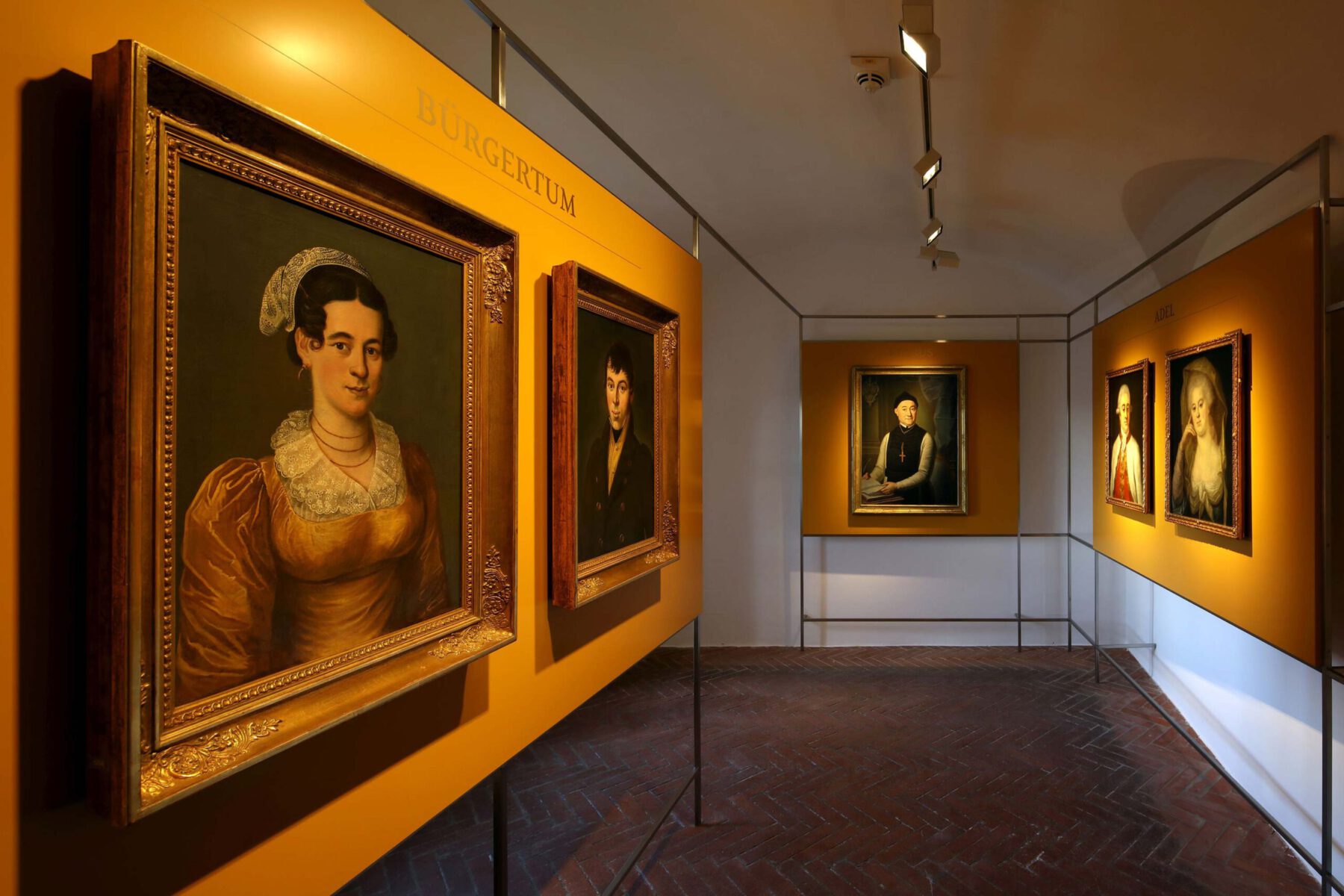 Raum mit gelben Stellwänden. Daran hängen historische Porträts von Frauen und Männern.